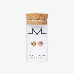 Rose gold dodecahedron shaped studs inside a glass tube with cork top on a white background by Matthew Calvin