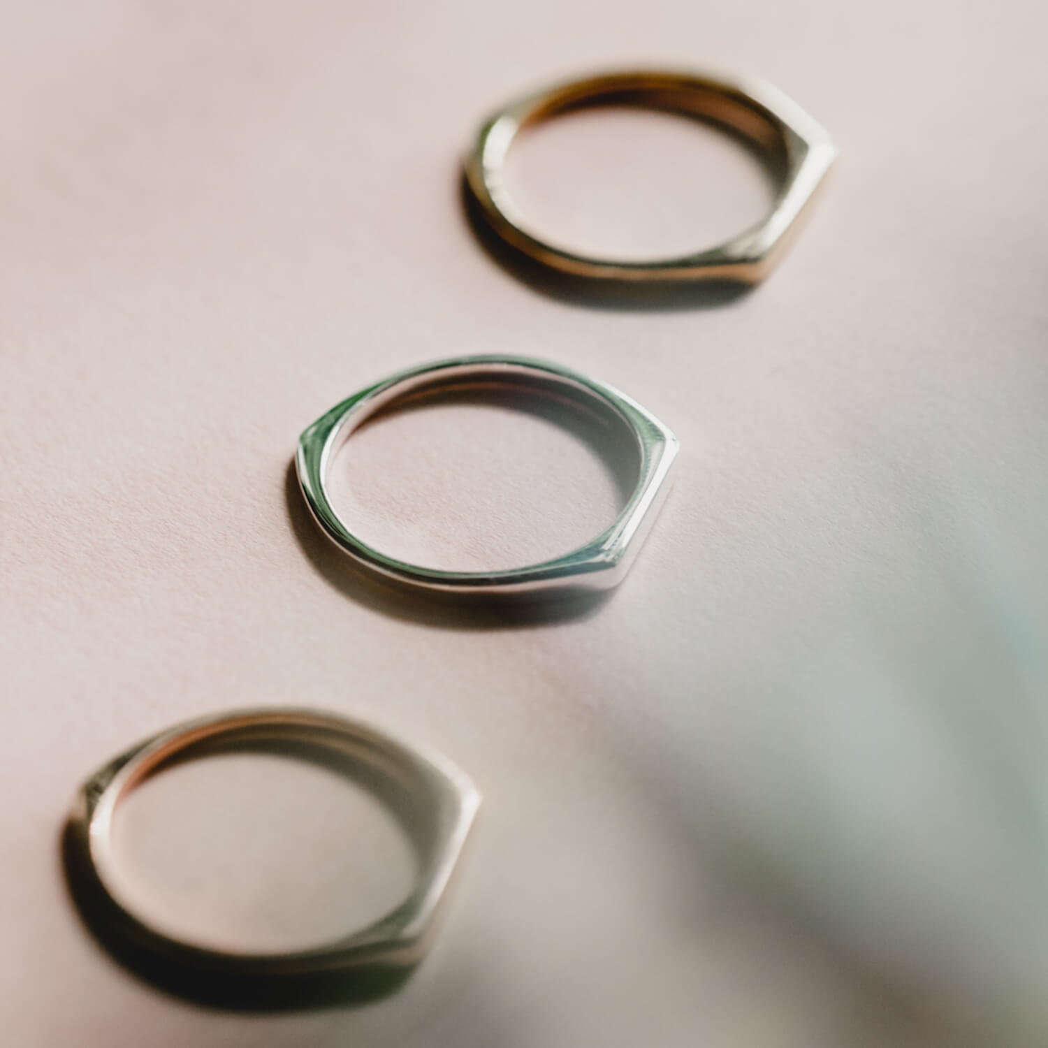 Close up of three thin signet rings, one in rose gold, one in gold and one in silver