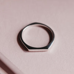 Close up of a thin silver signet style ring with a point at the bottom