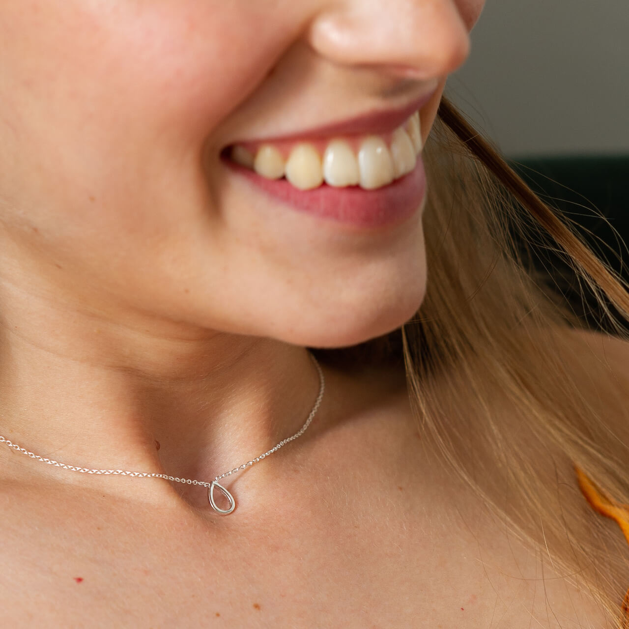 Close up of a woman wearing a silver necklace with a teardrop shaped charm