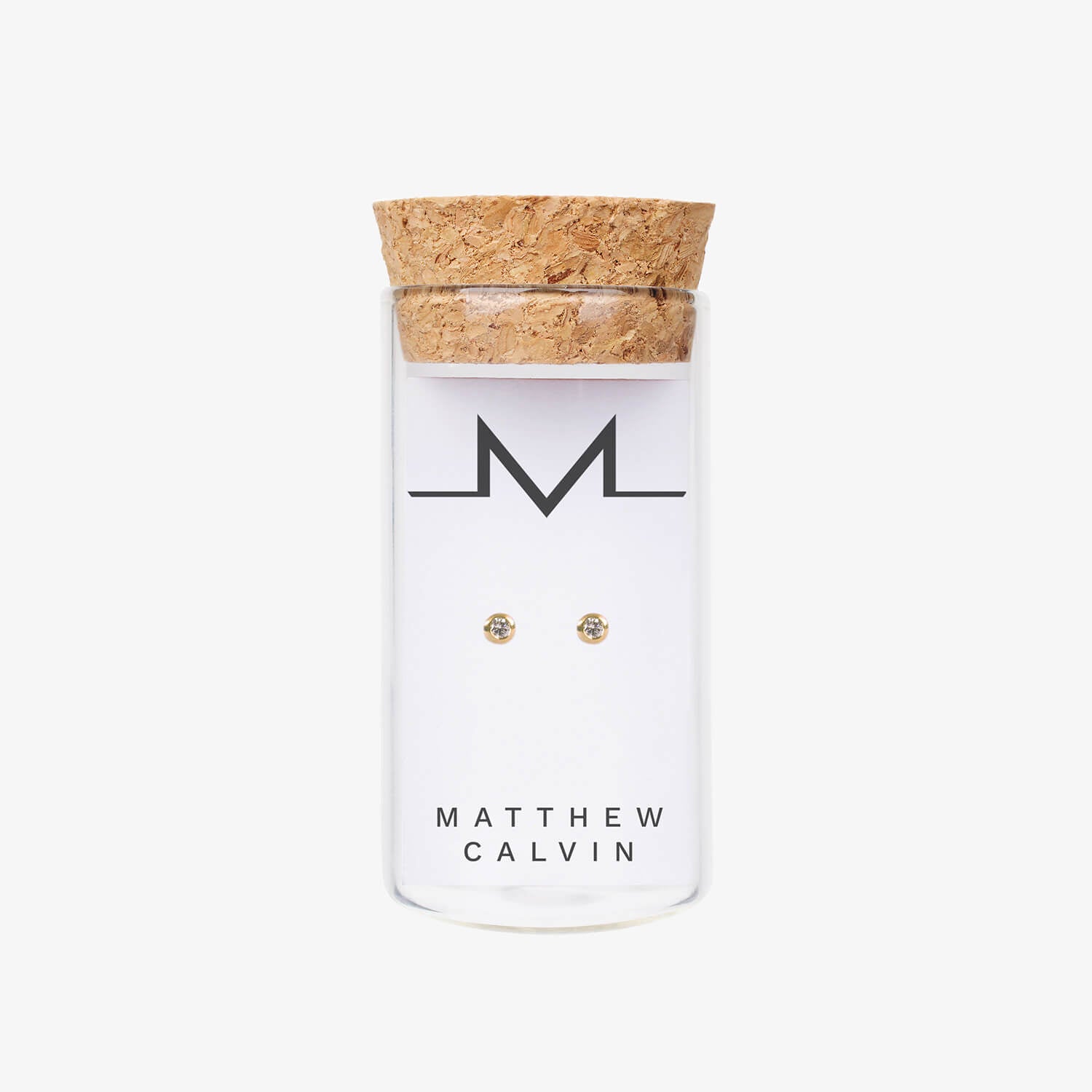 Matthew calvin gold diamond tiny tube studs presented in a glass bottle with cork topper on a white background