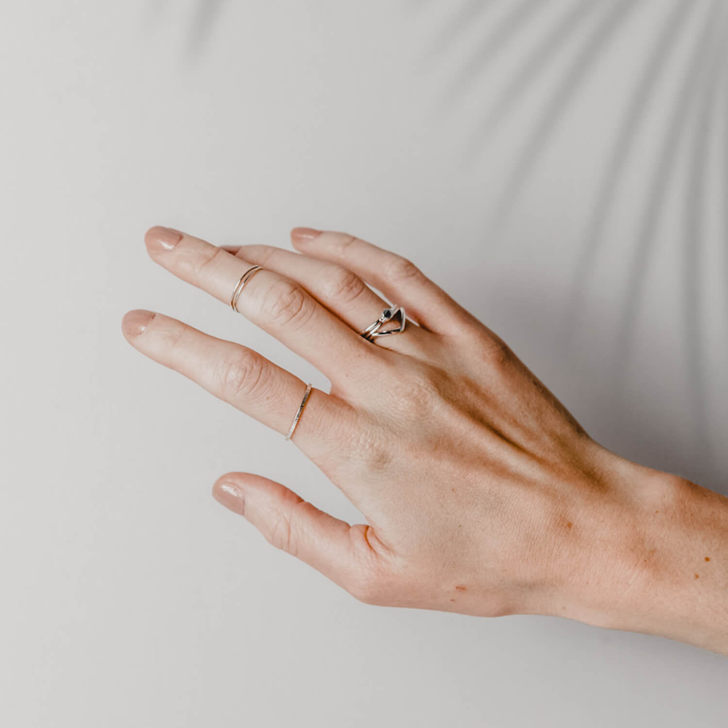 Close up of a hand wearing several silver rings in different styles