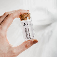 A hand holding a small glass bottle with cork lid, which contains long bar earrings in silver with textured detailing