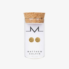 A glass bottle with a cork lid which has round gold earrings displayed in it