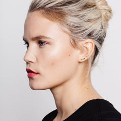 A woman wearing a pair of small square studs with textured finish