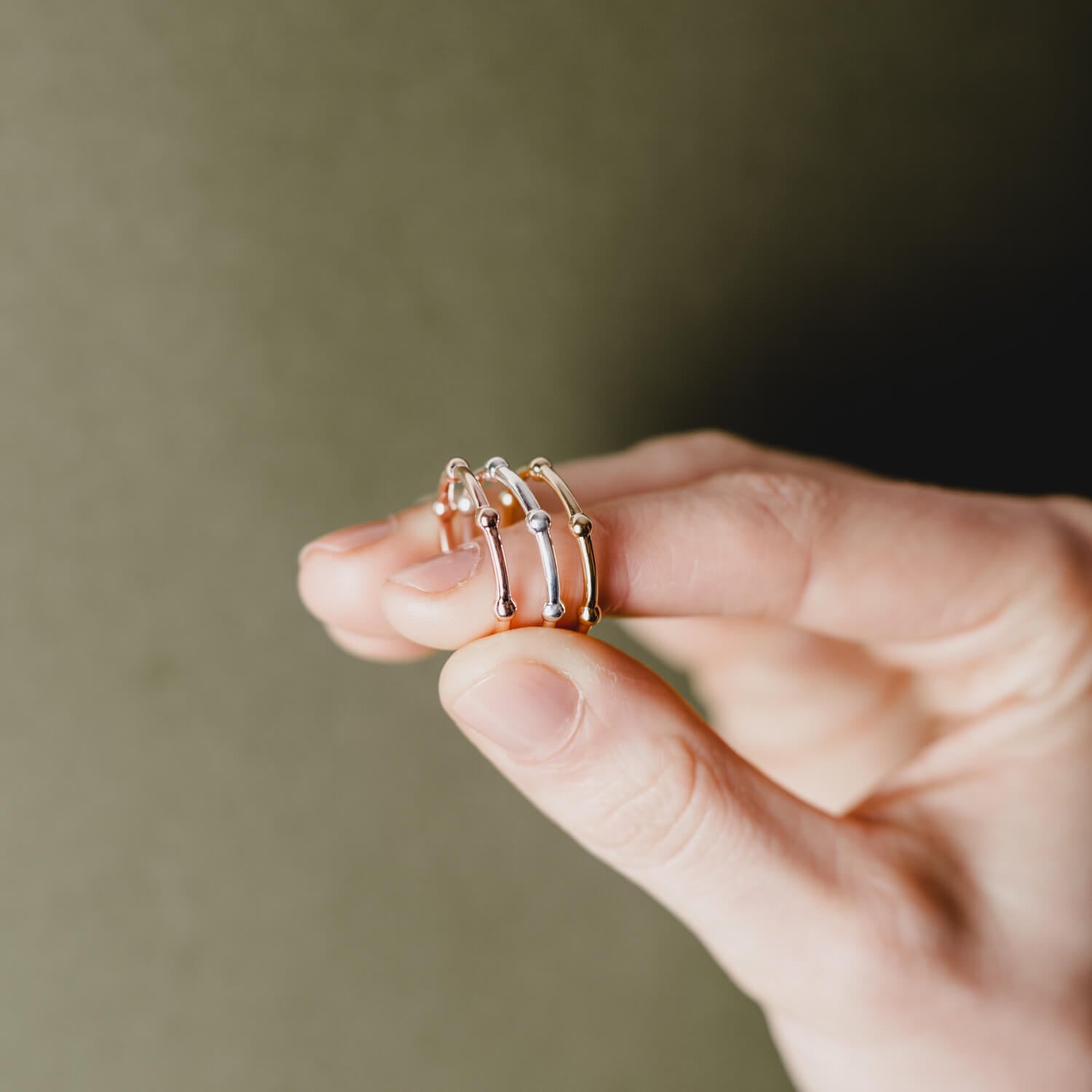 A close up of a hand holding three rings made from beaded wire, one gold, one silver and one rose gold