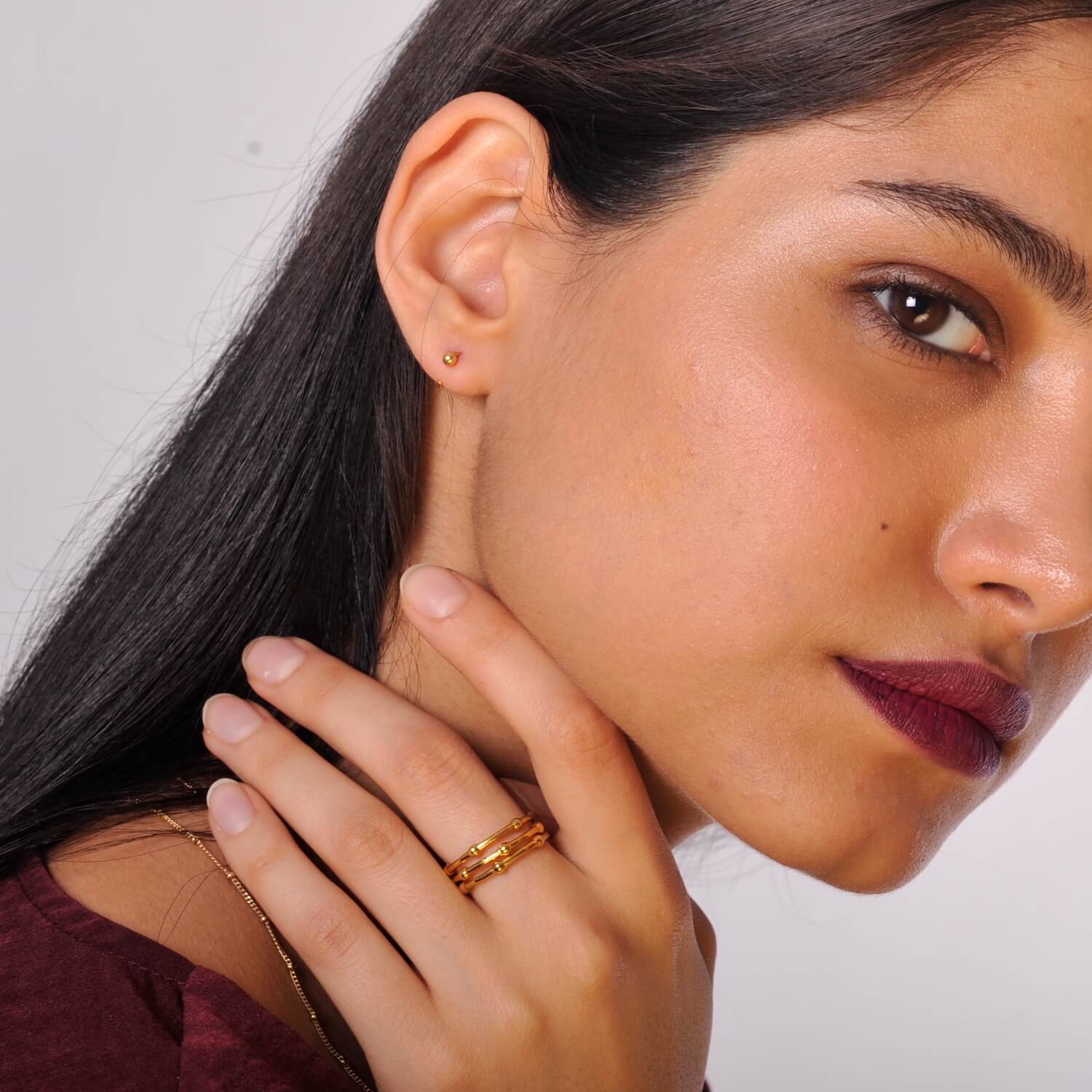 Close up of a model wearing small gold stud earrings and three gold rings