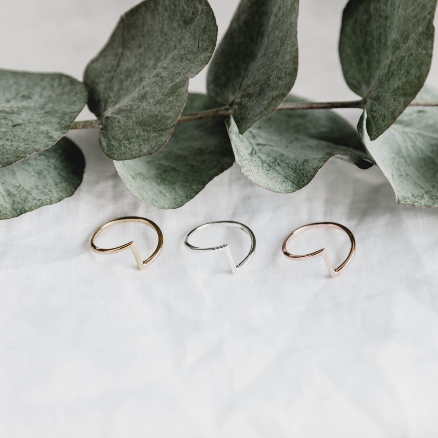 Trio of Matthew Calvin joint rings in gold, rose gold and silver with green eucalyptus leaves