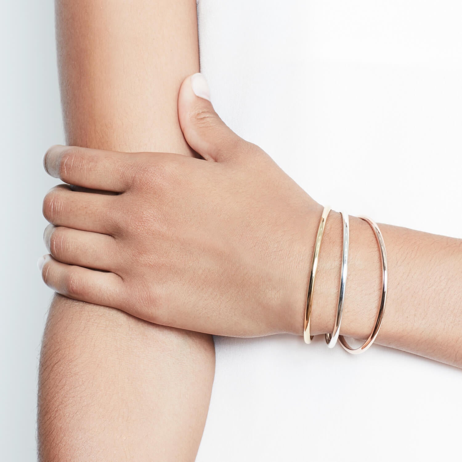 Close up of a model wearing three bangles, one silver, one rose gold and one gold