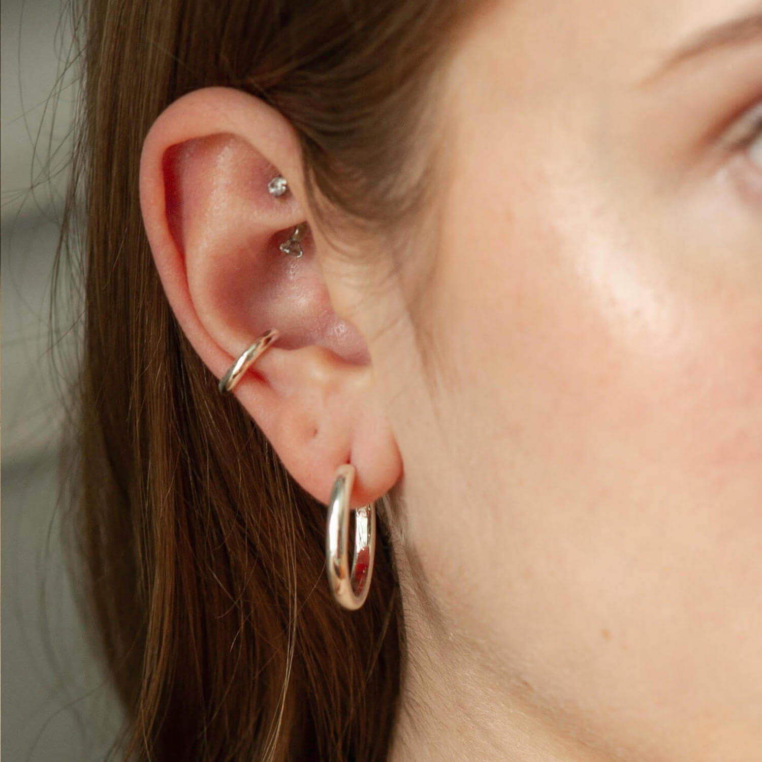 Close up of woman wearing a big silver hoop, a small silver ear cuff and two diamond studs