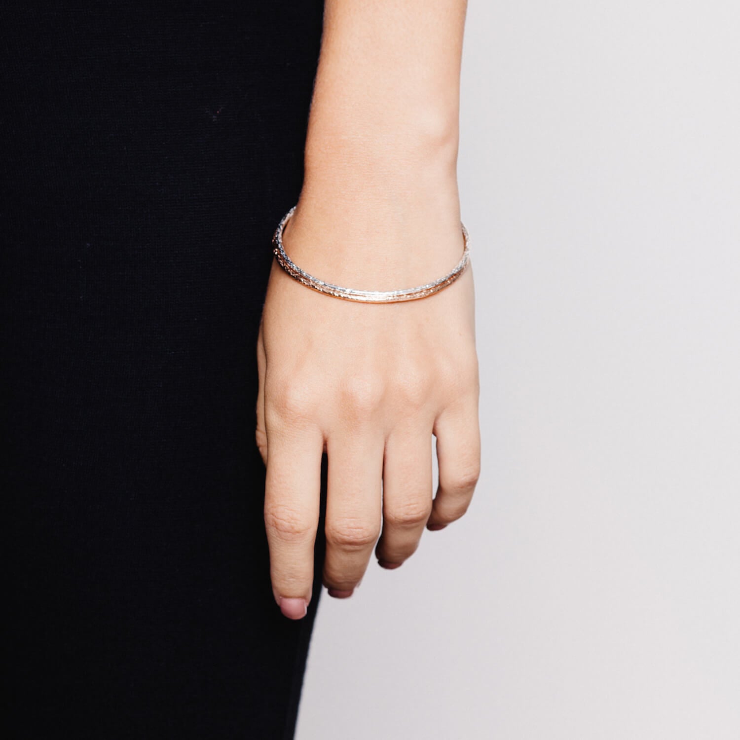 Model wearing two thin bangles with rough meteorite style texturing, one in silver and one in rose gold
