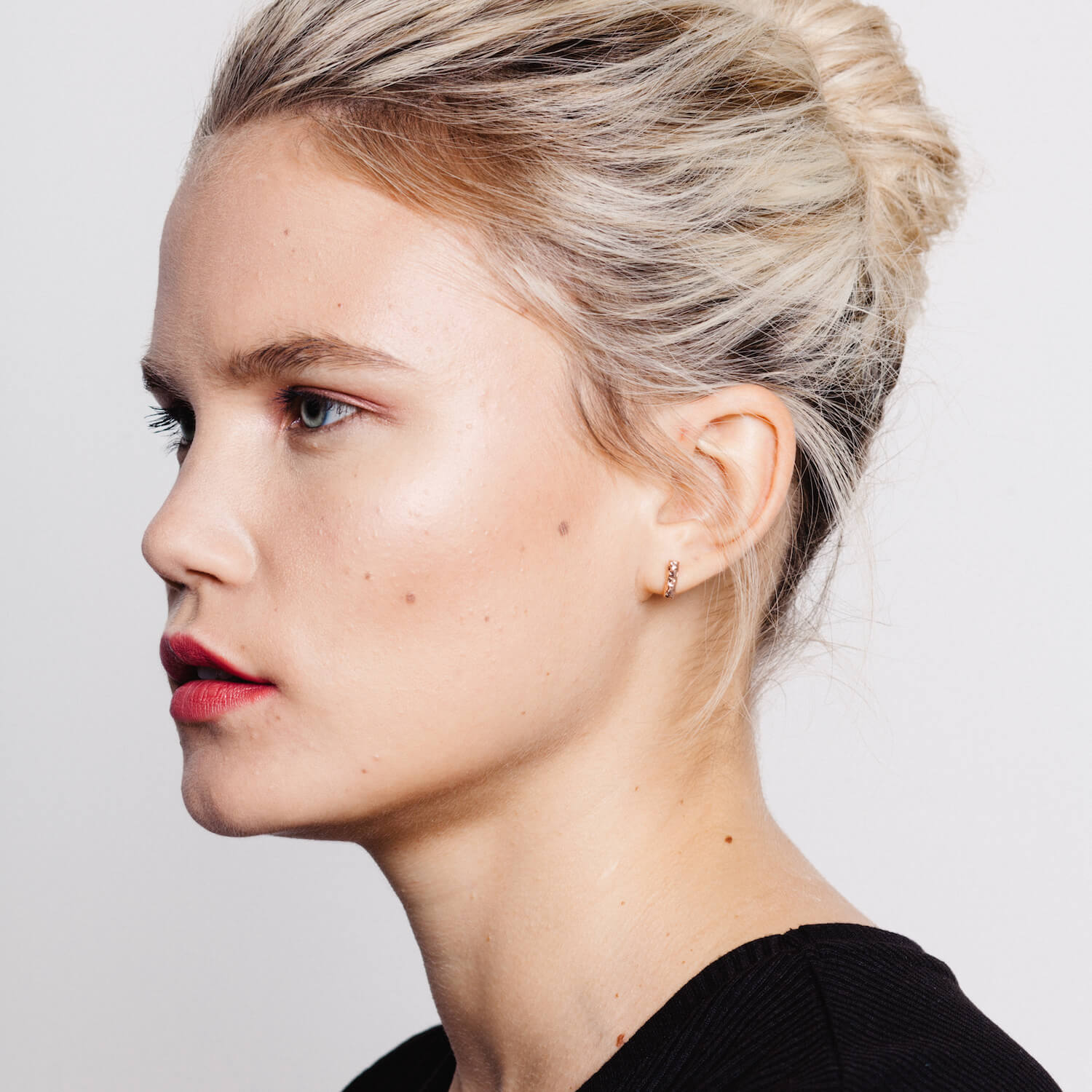 A woman wearing small bar earrings with a textured meteorite style design