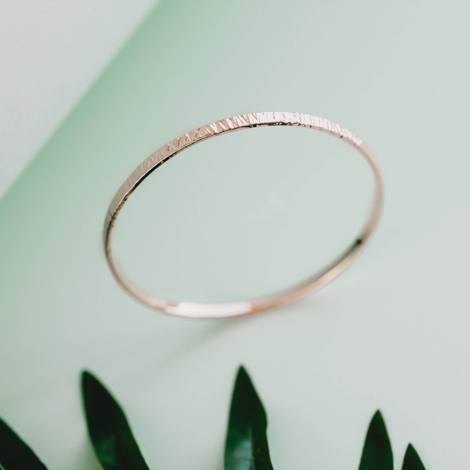 Silver bangle with a textured finish on a green background