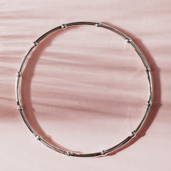 Silver bangle made from beaded wire on a pink background