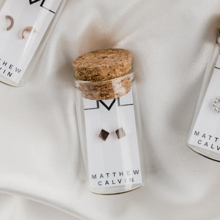 gold vermeil cube square stud earrings by matthew calvin presented in a glass tube with cork topper on a white satin background