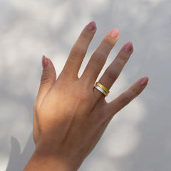 A model's hand with two textured rings, one in gold and one in silver