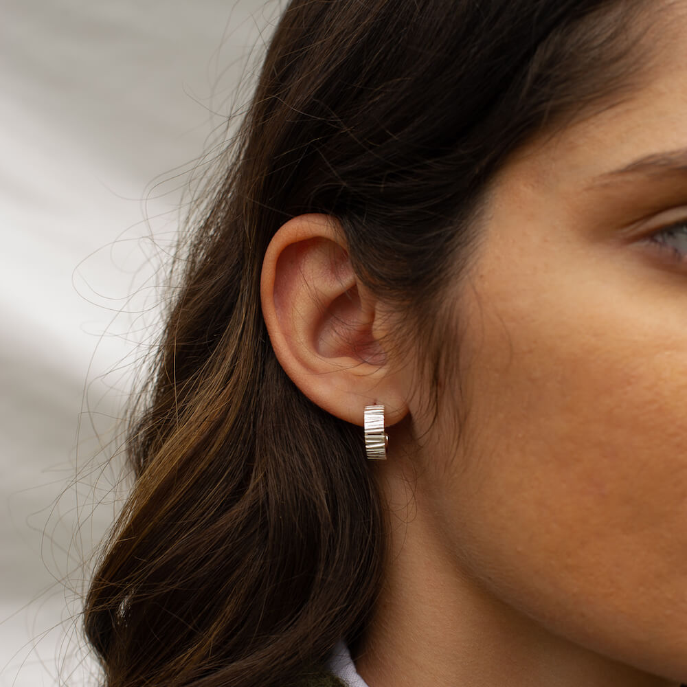 A model's ear with a silver textured hoop in it