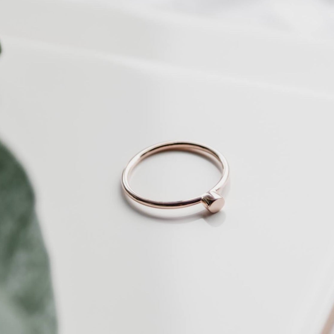 Rose Gold Matthew Calvin simple dot ring photographed on a white background with greenery