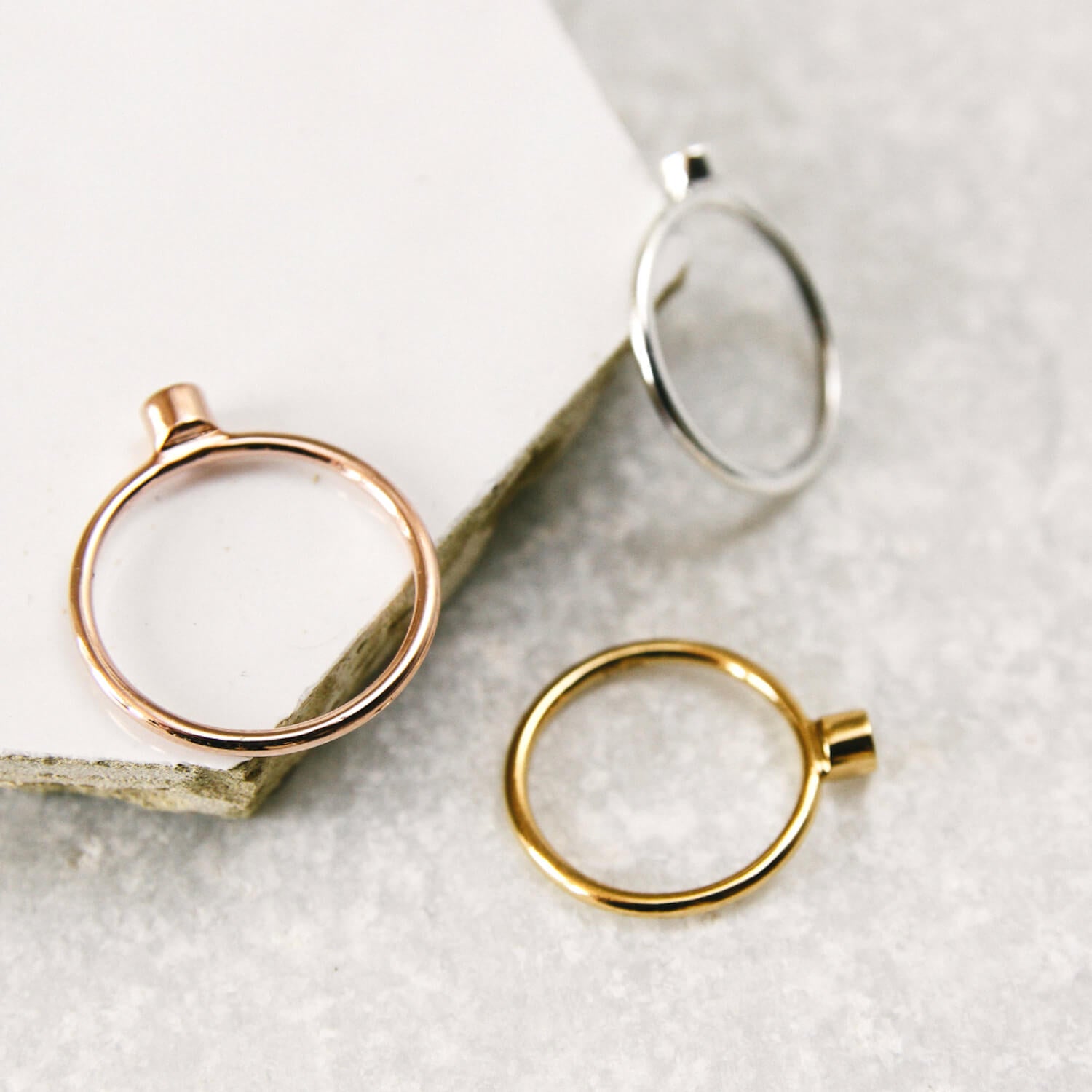Three rose gold, silver and gold Matthew Calvin simple dot rings photographed on a hexagonal tile 