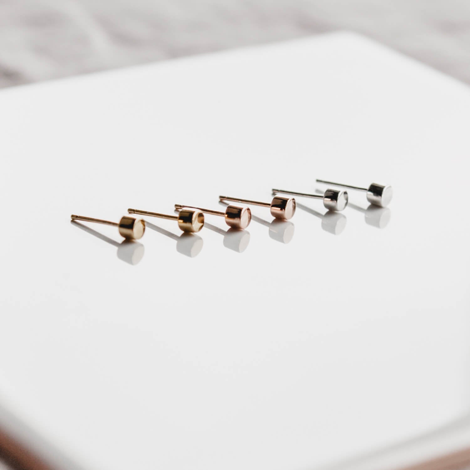 Simple silver, gold and rose gold Matthew Calvin dot stud earrings in a row on a white tile