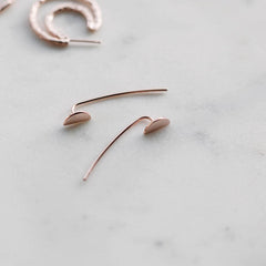 Close up of rose gold dropback earrings with a disc shaped charm