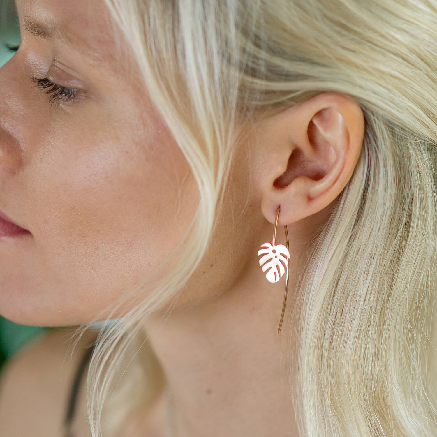 A model wearing a gold dropback earring with monstera charm