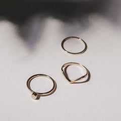 Close up of several rings on a white background, one with a small round charm, one with chevron detail and one thin plain band