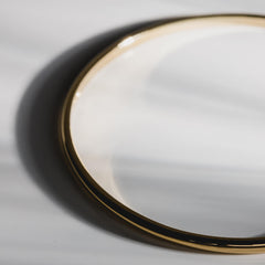 Close up of a plain gold bangle on a white background