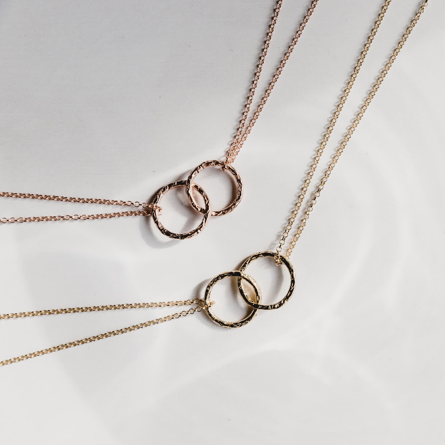 Close up of two pendants with intertwined rings, one in gold, one in rose gold