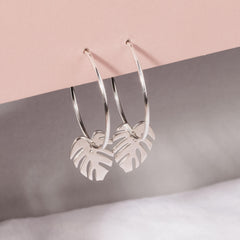 Close up of silver hoops with monstera leaf charms