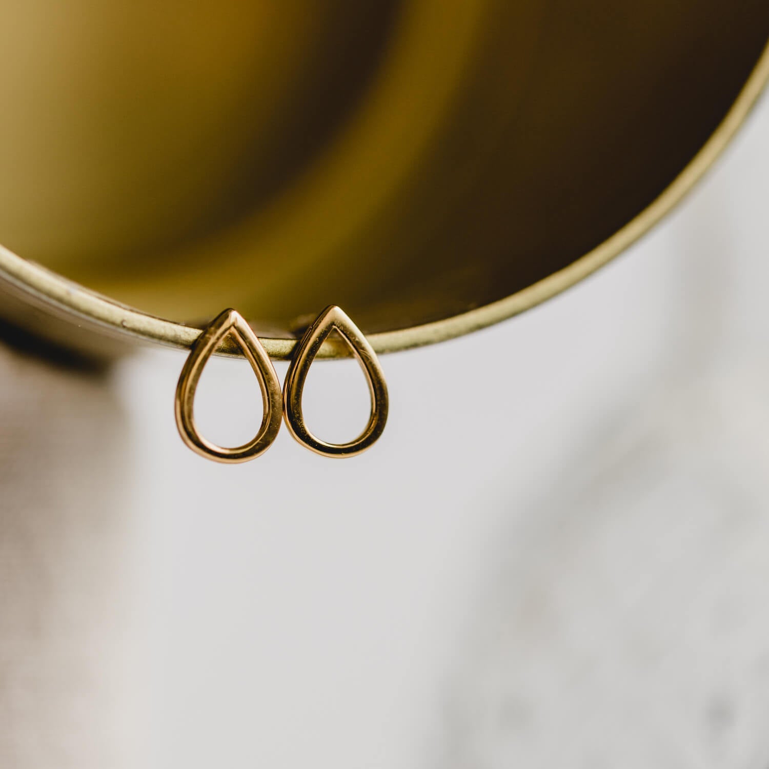 Close up of gold teardrop shaped earrings hung on a gold tube