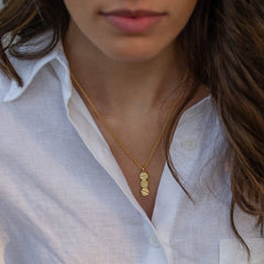 A model in a white shirt with a gold textured pendant on a chain