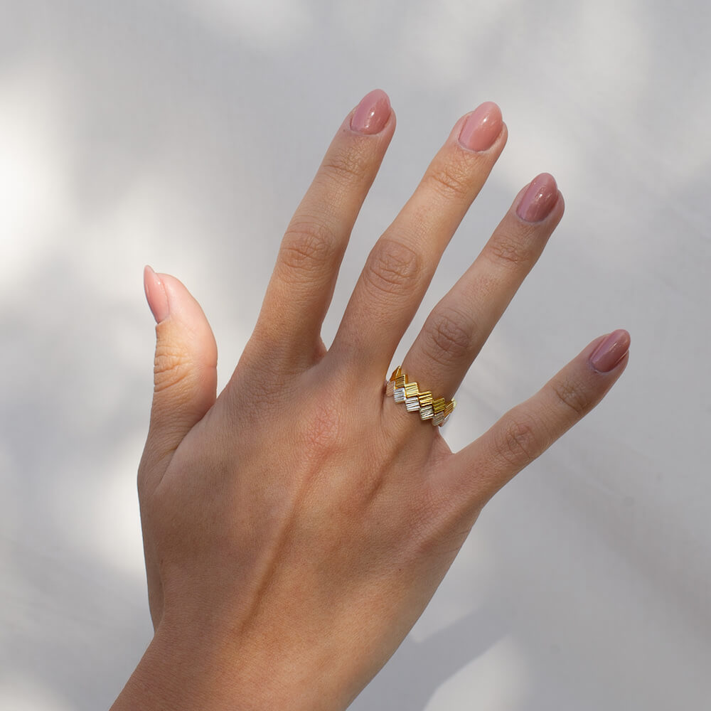 Model's hand in dappled sunlight wearing two geometric rings, one in silver and one in gold