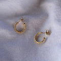 Small gold textured huggy hoops on a rough cloth background