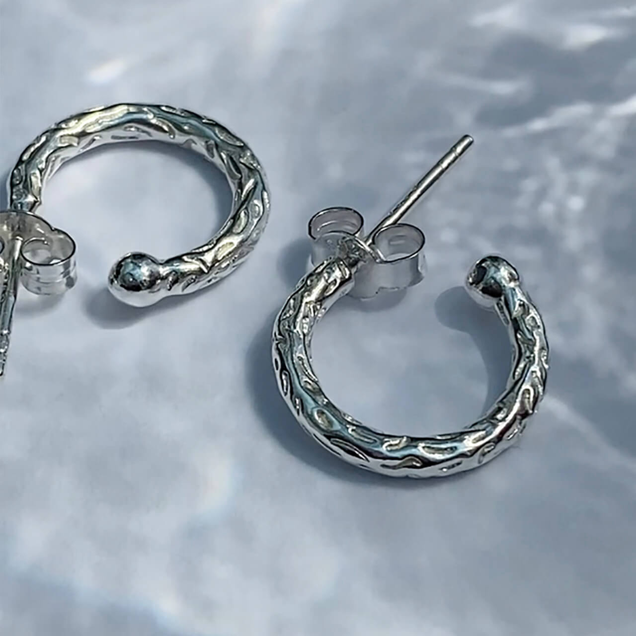 Close up of silver huggy hoops with a meteorite style texture