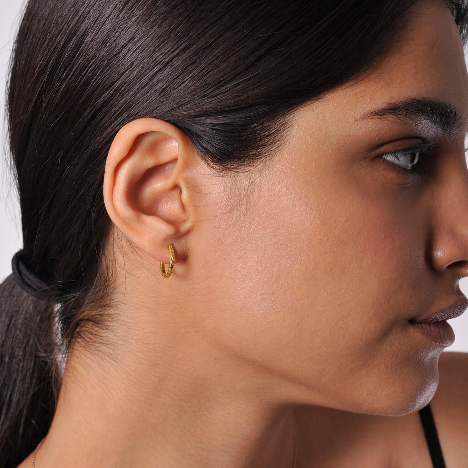 Model wearing small gold huggy hoops with a textured finish