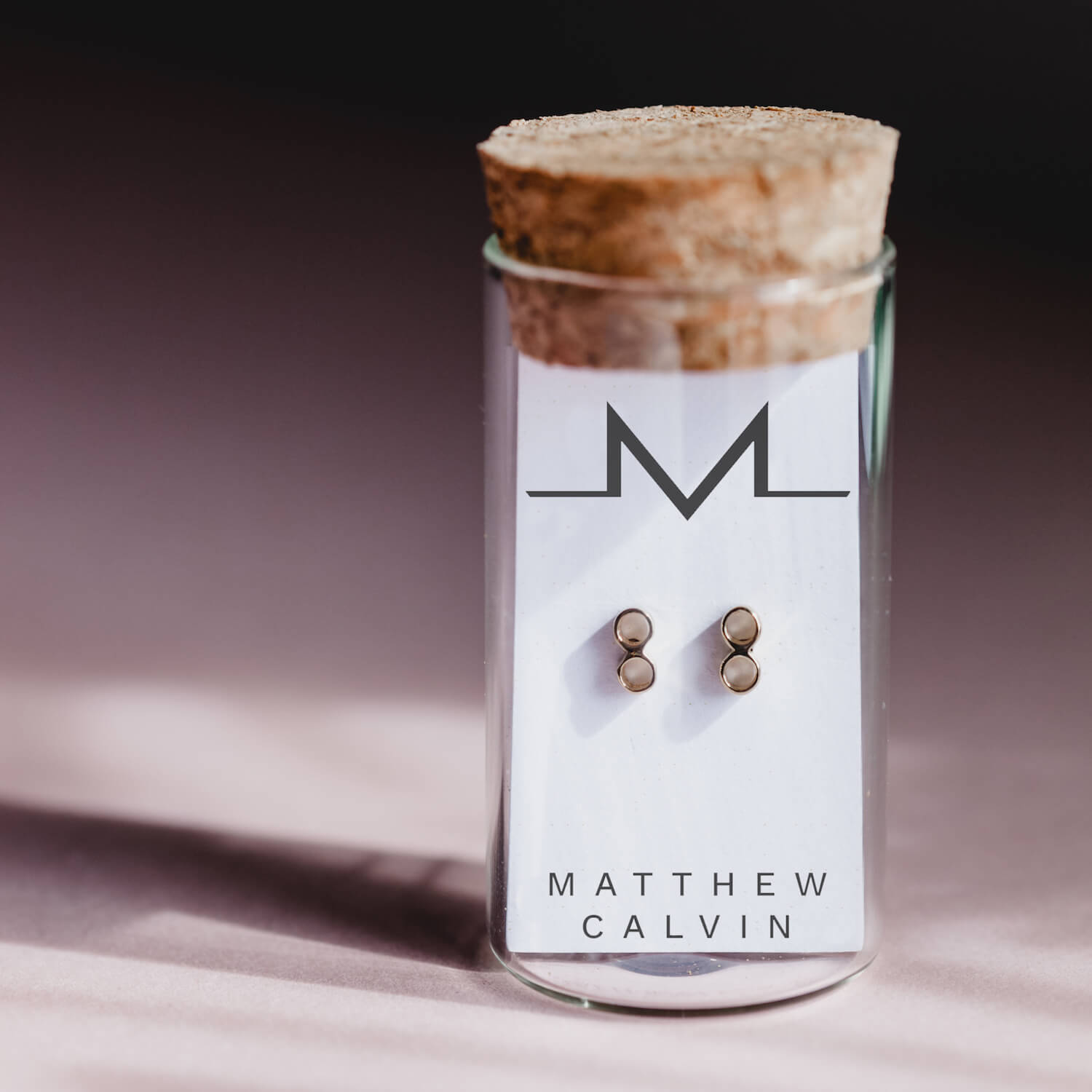 Close up of Matthew Calvin glass tube with cork stopper, featuring gold tiny double tube stud earrings