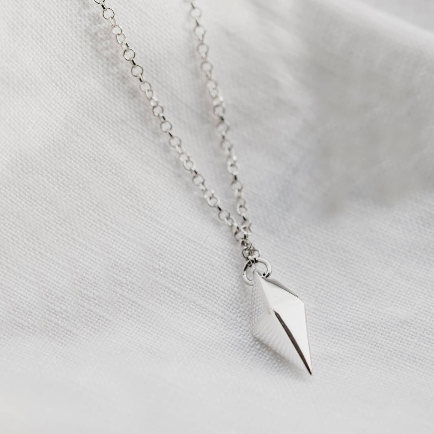 Close up of a silver pendant with a kite shaped charm